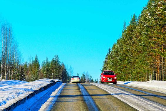 Kaksi autoa ajaa maantiellä sulassa talvimaisemassa